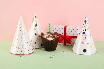 Birthday cupcake, gift box and party hats on color background