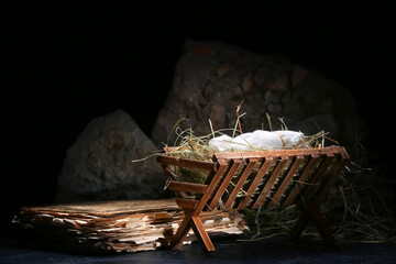 Manger with baby, hay, old book and stones on table against dark background