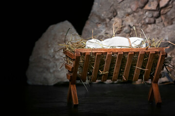 Manger with baby, hay and stones on dark background