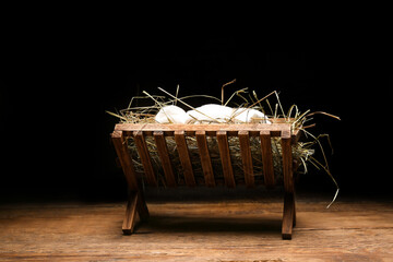 Manger with baby and hay on wooden table against dark background