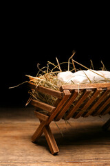 Manger with baby and hay on wooden table against dark background, closeup