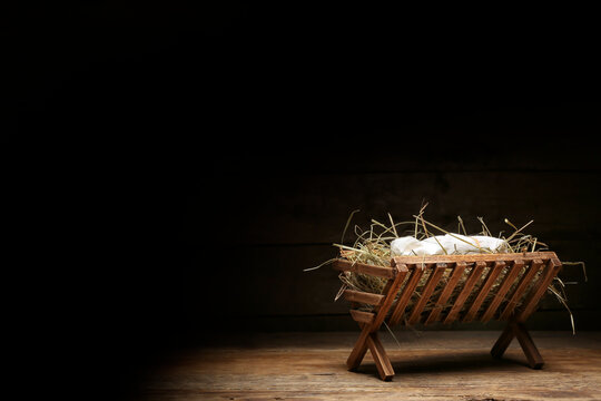 Manger with baby and hay on wooden table against dark background