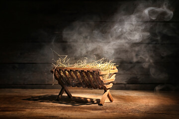 Manger with hay and smoke on dark wooden background