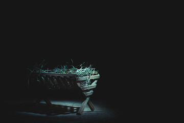 Manger with hay on table against dark background