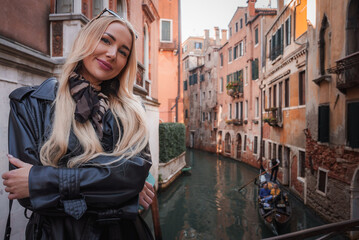 Fototapeta na wymiar A woman in a leather jacket poses on a bridge in Venice, Italy, enjoying the city's canals. The overall vibe is casual and relaxed.