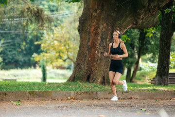 Athletic strong blonde runner woman in headphones jogging in park.