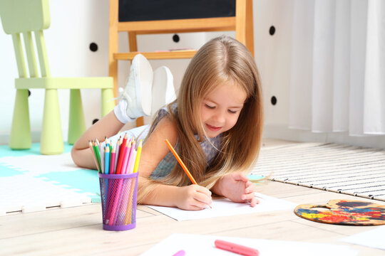 Cute little girl drawing with pencils on floor at home