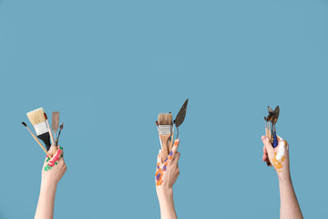 Female hands with paintbrushes and palette knives on blue background