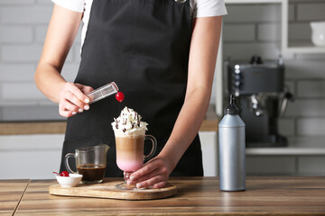 Female barista decorating tasty coffee on wooden table in kitchen