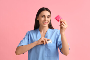 Female gynecologist with condoms on pink background