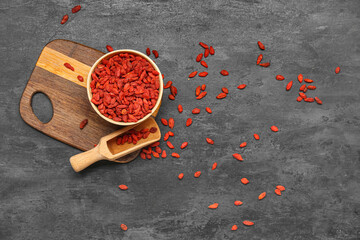 Bowl and scoop with red dried goji berries on black background