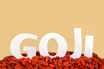 Word GOJI and red dried berries on yellow background