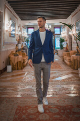 A stylish man in a blue blazer walks through a luxurious Venetian-style hotel lobby. The elegant...