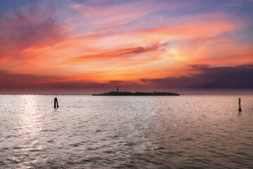 Aerial view of serene sunset over calm water with small island in distance. Warm glow, picturesque clouds, and smooth water surface create a stunning and peaceful scene.