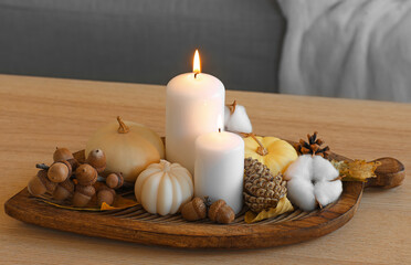 Fototapeta na wymiar Wooden board with burning candles and beautiful autumn decor on table in room, closeup