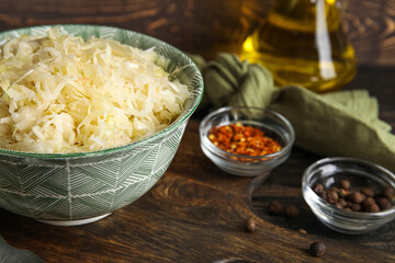 Bowl with delicious sauerkraut and different spices on wooden background