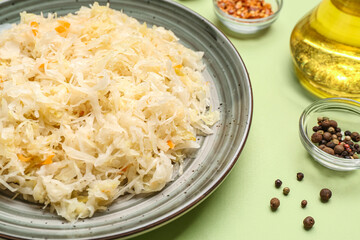 Plate with tasty sauerkraut with spices on green background