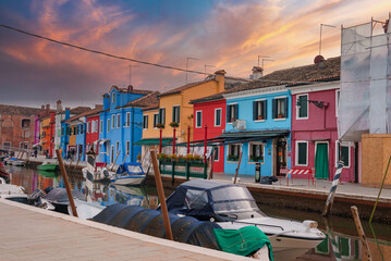 A boat is docked in front of a colorful building, on the Burano island, Italy. The image captures a typical scene in the city, adding to its charm and beauty.