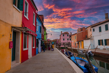 Colorful houses line a canal in Burano, Italy. The specific location and angle are unknown. No boats or gondolas are visible. Predominant colors, materials, and atmosphere are unspecified.