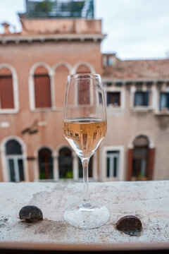 A glass of pink wine overlooks a serene and picturesque cityscape of traditional Venetian-style buildings. The image captures a luxurious and relaxing atmosphere in Venice, Italy.