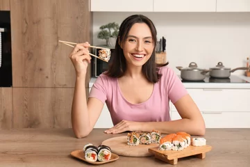 Fotobehang Happy young woman eating tasty sushi rolls in kitchen © Pixel-Shot
