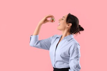 Happy young woman eating tasty maki roll on pink background