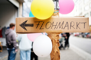 a sign hand-written on cardboard with the inscription flea market on a lamppost with balloons in an...
