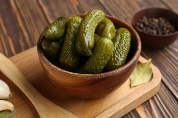 Board with bowl of tasty pickled cucumbers and different spices on wooden background