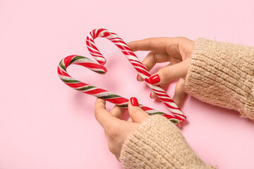 Female hands with red manicure and Christmas candy canes on pink background