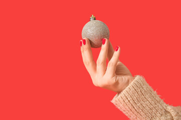 Female hand with red manicure holding Christmas ball on color background