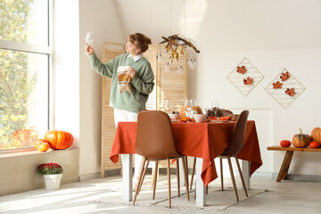 Beautiful young woman decorating table for Thanksgiving dinner in modern dining room