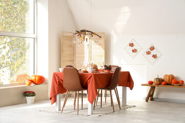 Autumn table setting with pumpkins and pine cones in light dining room
