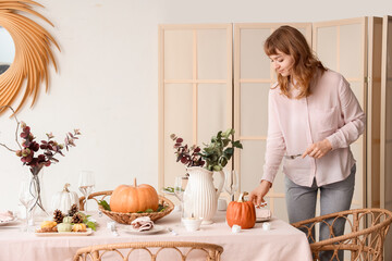 Beautiful young woman decorating table for Thanksgiving Day dinner in dining room