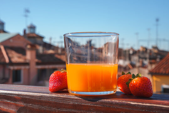A refreshing glass of orange juice with strawberries sits on a neutral-toned balcony. This image is part of a collection showcasing popular places in Venice, Italy.