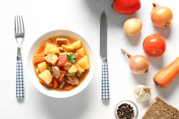 Bowl with delicious beef stew and different ingredients on white background