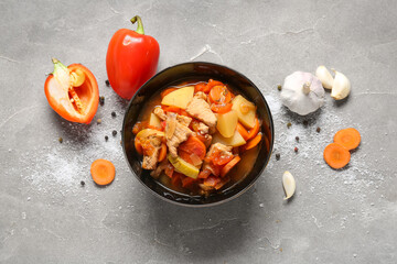 Black bowl with delicious beef stew and different ingredients on grey background