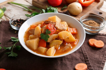 Bowl with delicious beef stew and ingredients on table, closeup