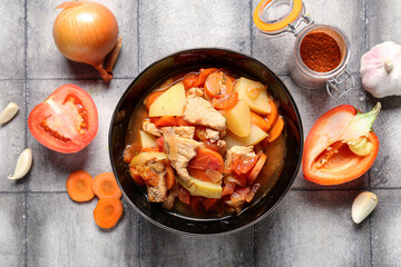 Bowl with delicious beef stew and different ingredients on grey tile background