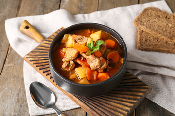 Black bowl with delicious beef stew and parsley on wooden background