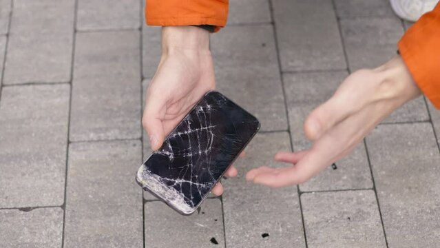 Crash smartphone on pavement and man picks it up holding a with a broken screen smartphone in his hand slow-motion footage 4K UHD B-Roll