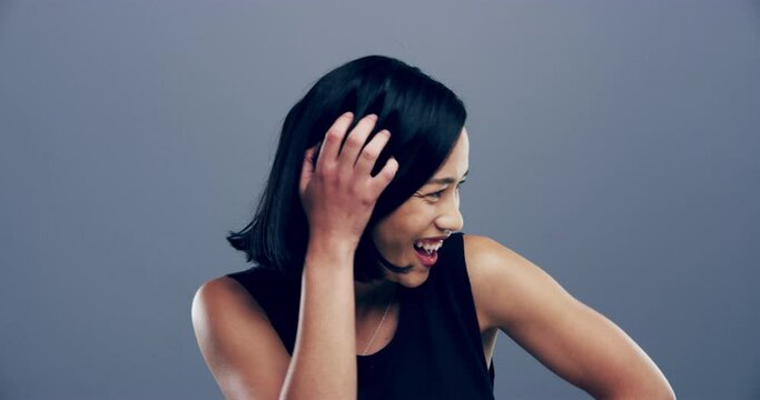 Asian, face and woman laugh in studio with funny joke, happiness or reaction to comedy. Happy, portrait and girl with comic, joy or lol emoji with humor and smile in grey background or mockup