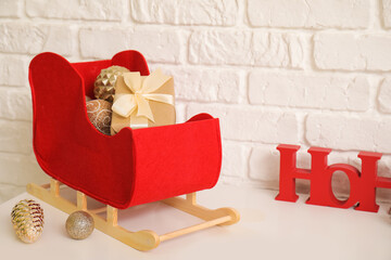 Obraz premium Decorative sleigh with Christmas decorations and gift box on table near light brick wall