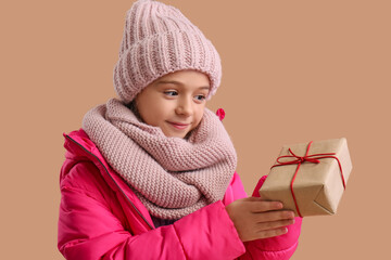 Cute little girl in winter clothes with gift box on beige background