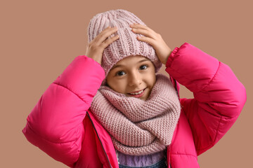 Cute little girl in winter clothes on beige background