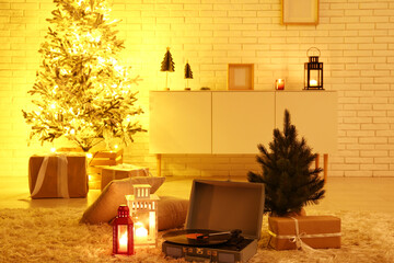 Record player, glowing lanterns and small Christmas tree on soft carpet in living room at evening