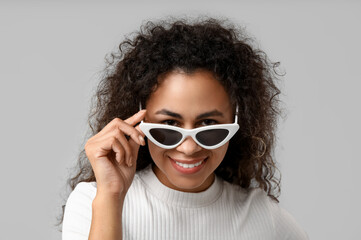 Stylish African-American woman in sunglasses on grey background, closeup