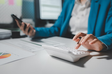 Female accountant working about financial with calculator at her office, Savings, Finances and economy concept, Beautiful Asian businesswoman analyzes charts using laptop calculator at the office.