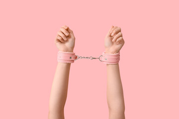 Female hands in handcuffs from sex shop on pink background