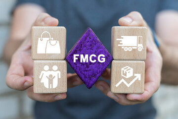 Man holding multi-colored blocks with icons sees on a purple rhombus the abbreviation: FMCG. Fast Moving Consumer Goods ( FMCG ) Digital Business Concept.