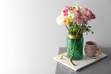 Bouquet of beautiful ranunculuses and tea on table near light grey wall. Space for text